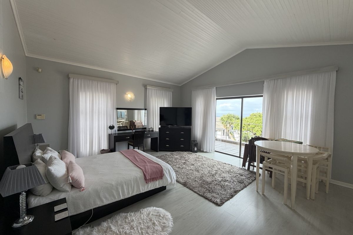 Spacious bedroom featuring vaulted timber ceilings, laminate flooring, and large sliding glass doors providing access to an outdoor balcony area.