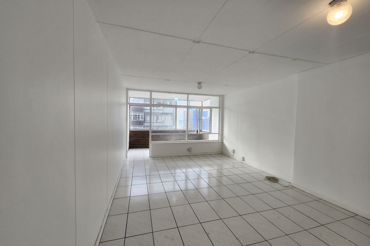 An empty, open-plan living area featuring white tiled flooring, a large window, and a neutral interior finish, ready for renovation or staging.