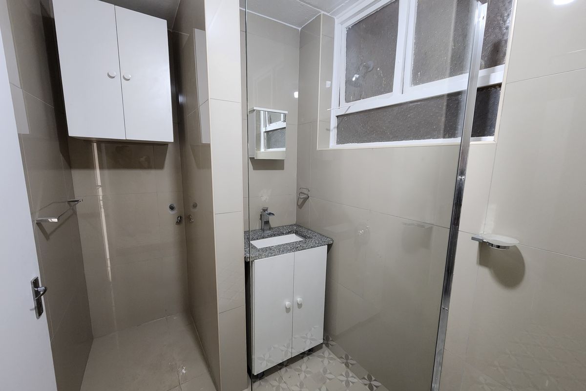 A clean, modern bathroom featuring a vanity with granite countertop, glass shower enclosure, and neutral wall tiling with patterned floor accents.
