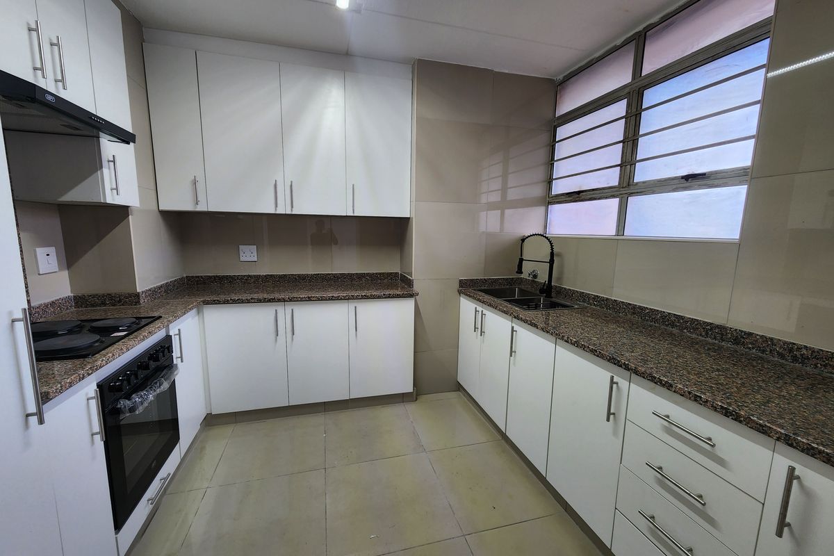 A clean, modern kitchen featuring white cabinetry, granite countertops, a built-in oven with hob, and a double sink with a contemporary mixer tap.