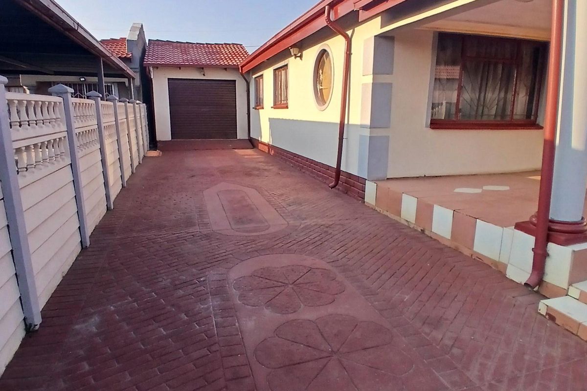 A side view of the property featuring a paved driveway, a detached garage, and a covered patio area with a boundary wall.