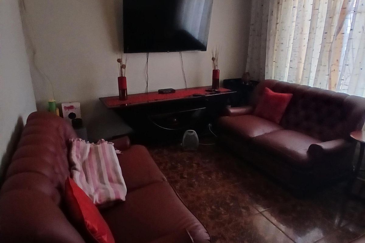 A cozy living room featuring tiled flooring and a textured ceiling, currently set up with a wall-mounted television.