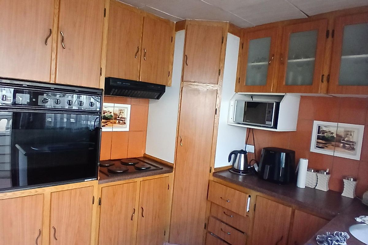 A dated kitchen featuring wood-finish cabinetry, built-in oven, electric hob, and tiled flooring, offering significant potential for a modern renovation.