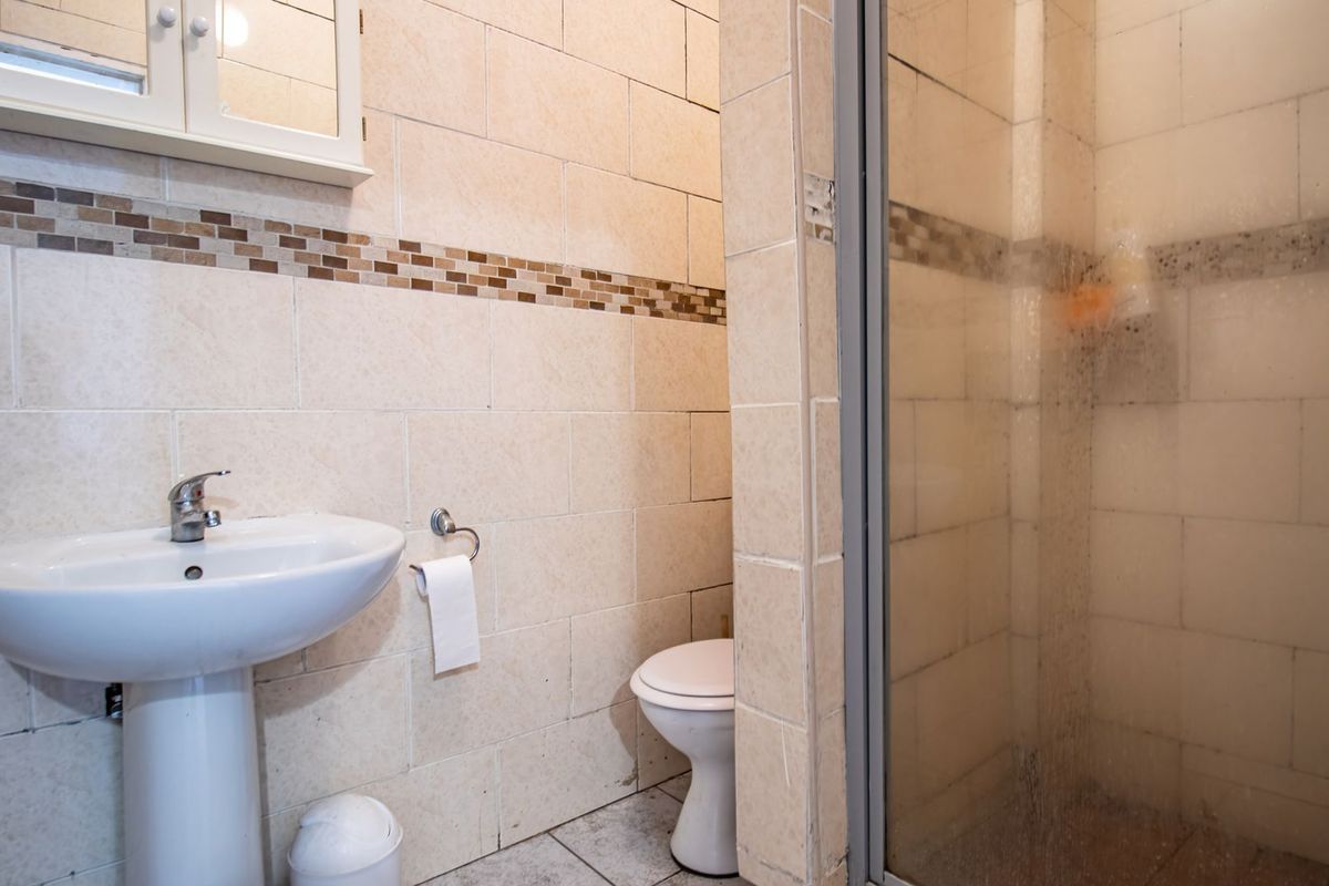 A functional bathroom featuring a pedestal basin, toilet, and a glass-enclosed shower with neutral wall and floor tiling.