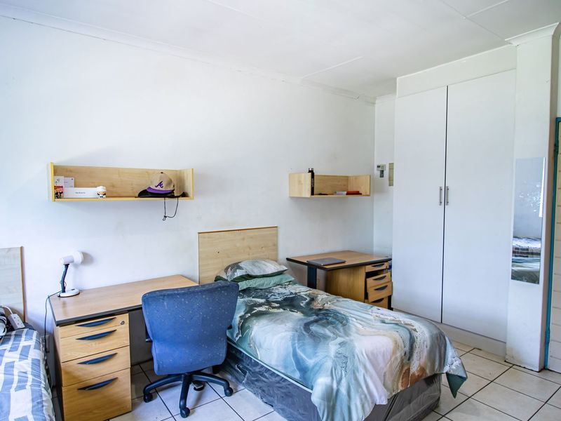 A functional bedroom featuring built-in wardrobe storage, wall-mounted shelving, and tiled flooring, offering a practical layout for a student or guest room.