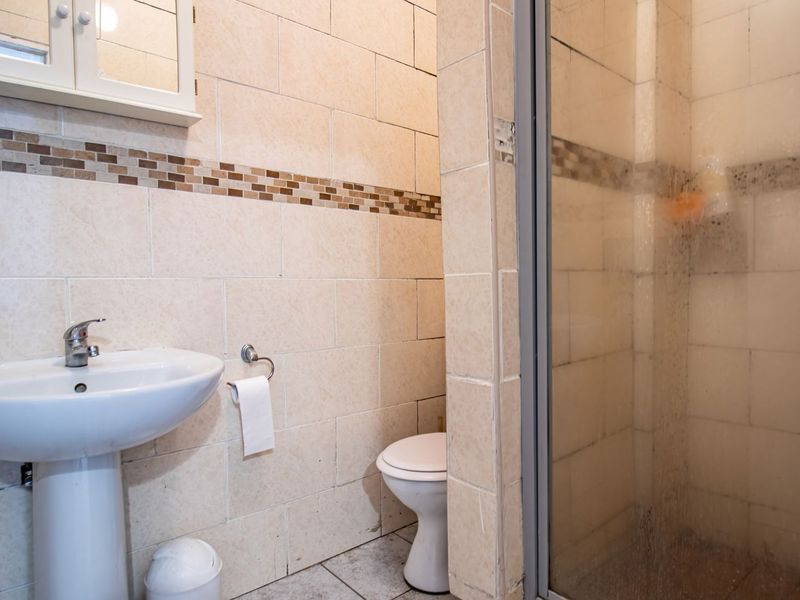 A functional bathroom featuring a pedestal basin, toilet, and a glass-enclosed shower with neutral wall and floor tiling.