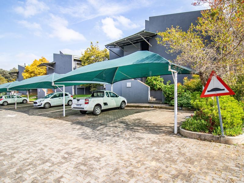Exterior view of the apartment complex parking area featuring covered shade cloth carports and paved driveway access.