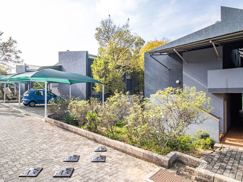 Exterior view of the apartment complex featuring paved driveway, shade cloth carports, and landscaped garden beds leading to the building entrance.