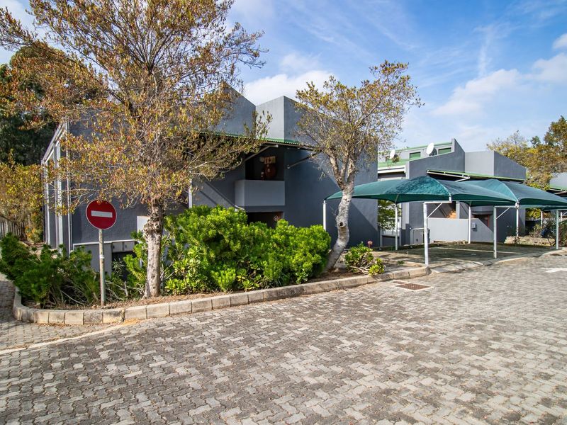 Exterior view of the apartment complex featuring a paved driveway, covered carport parking, and established garden landscaping.