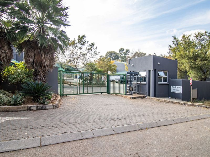 The entrance to Masingita Village features a secure gated access point with a guard house, turnstile, and paved driveway.