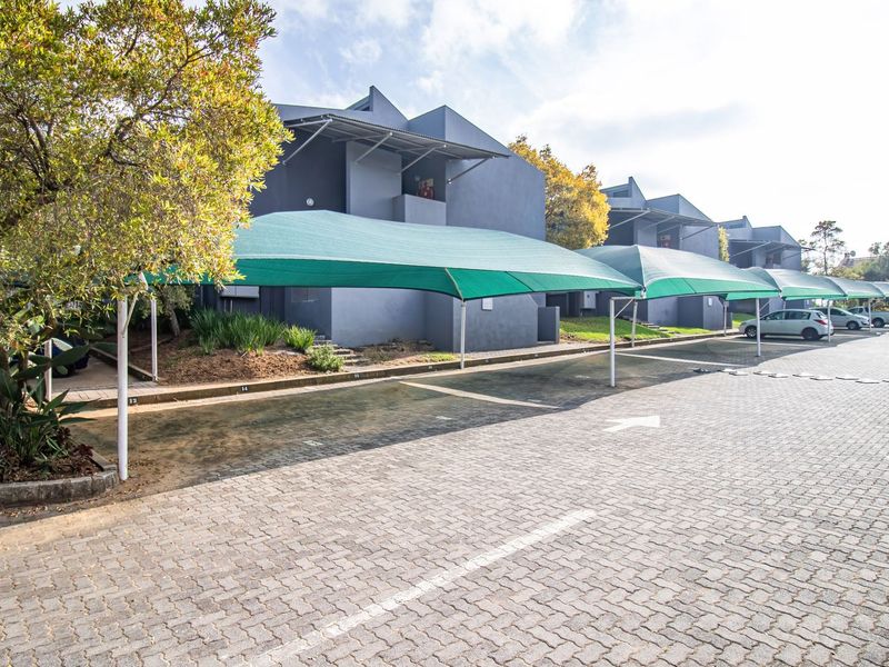 Exterior view of the apartment complex featuring paved parking areas with installed shade cloth carports and established garden landscaping.