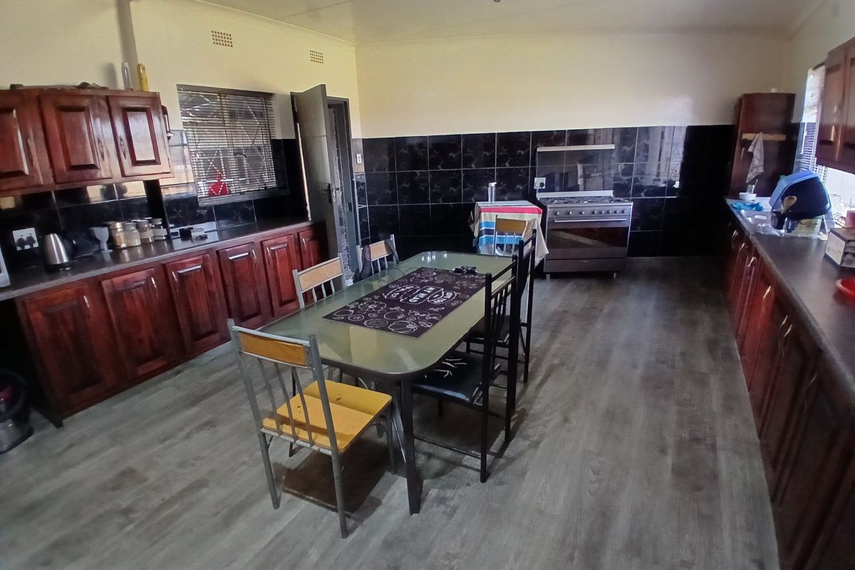Spacious kitchen featuring dark wood cabinetry, black tiled backsplash, laminate countertops, and a freestanding stove with ample space for a dining area.