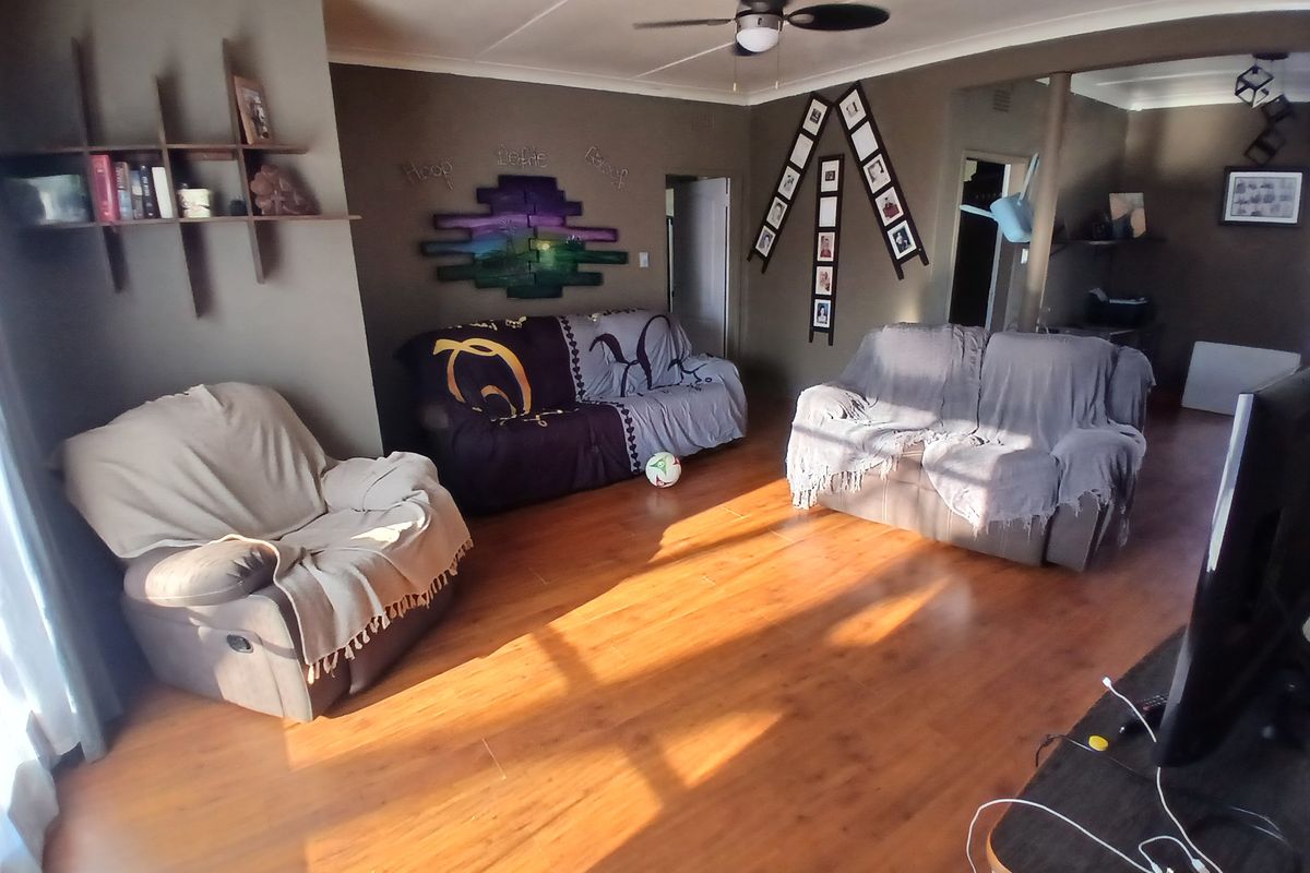 A spacious living room featuring warm-toned laminate flooring, a central ceiling fan, and coved cornicing, offering a comfortable and functional family living space.