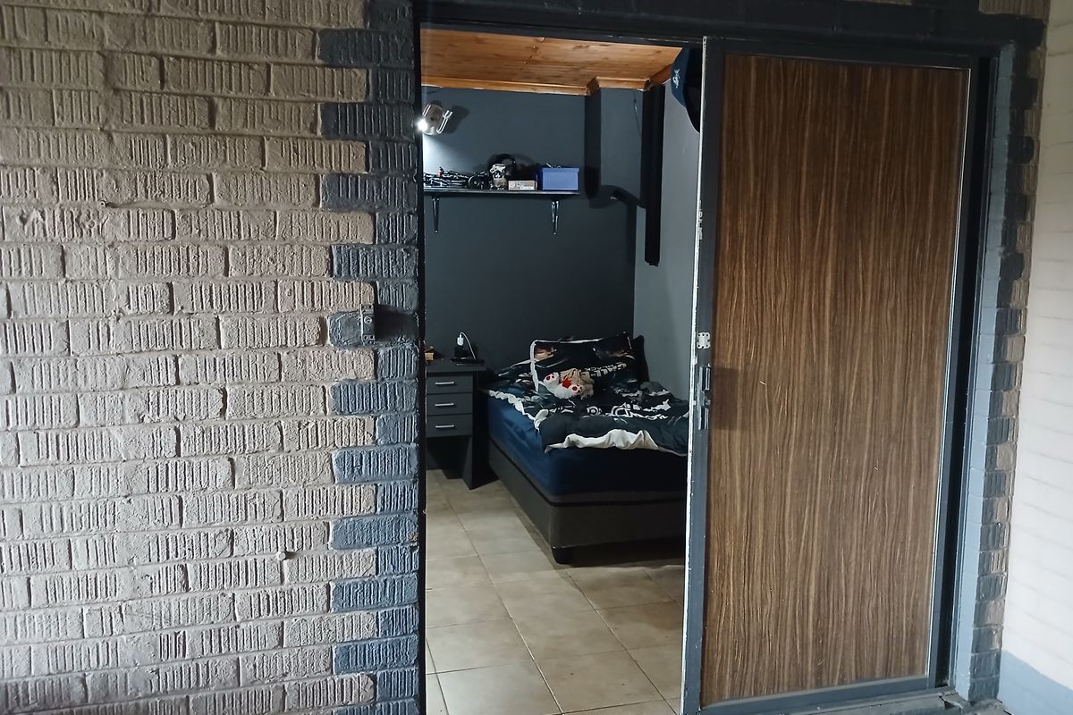 A bedroom featuring tiled flooring, a timber ceiling, and direct access via a sliding glass door from an exterior brick-walled area.