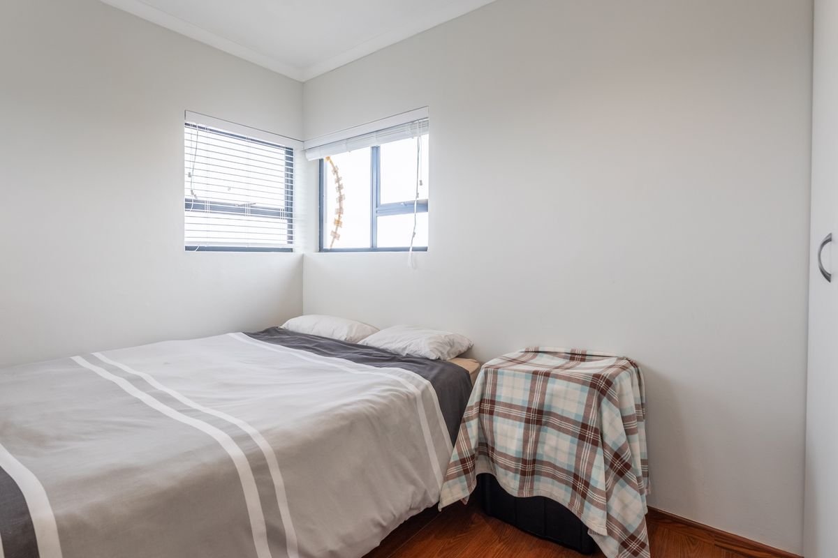 A compact bedroom featuring neutral walls, timber-look flooring, and built-in wardrobe storage.