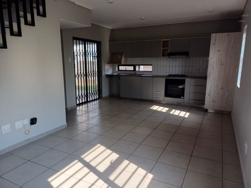 Open-plan kitchen and living area featuring tiled flooring, modern cabinetry, built-in oven and hob, and direct access to the exterior through a security gate.