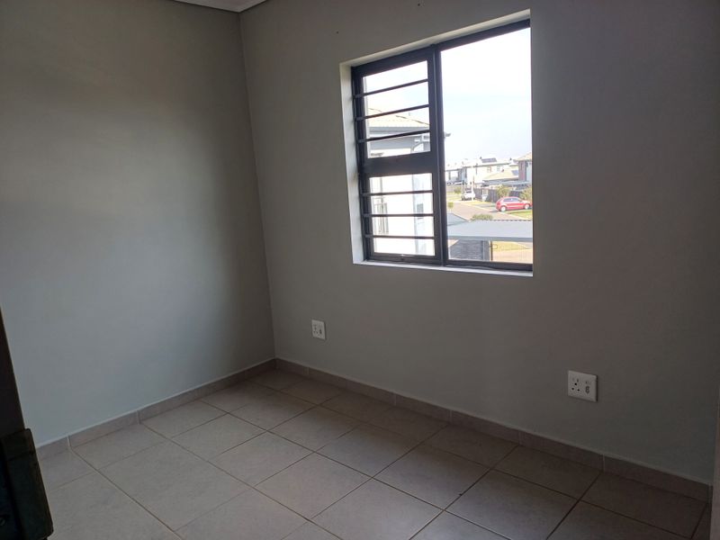 A clean, empty bedroom featuring neutral grey walls, tiled flooring, and a window fitted with security bars.