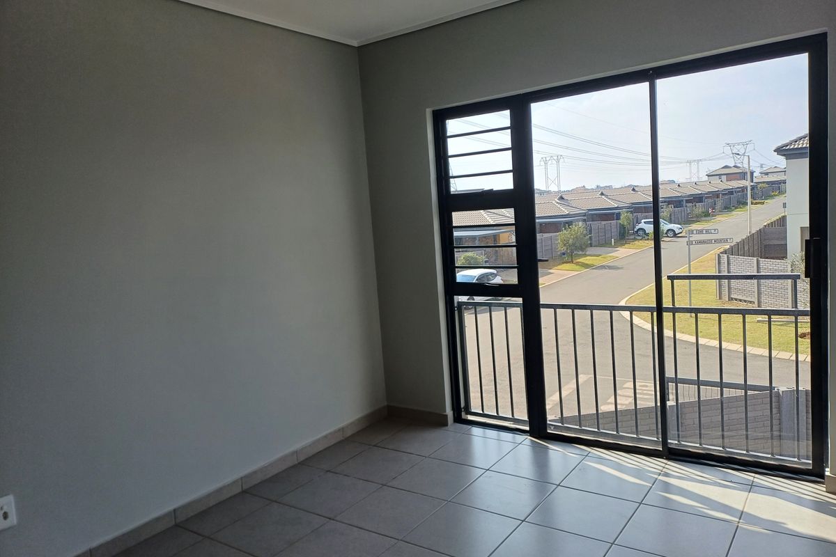 A bright, empty room featuring neutral tiled flooring and a large sliding glass door that opens onto a balcony with a neighbourhood view.