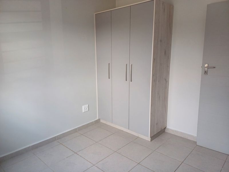 A clean, modern bedroom featuring neutral tiled flooring and a built-in wardrobe with light grey cabinetry.