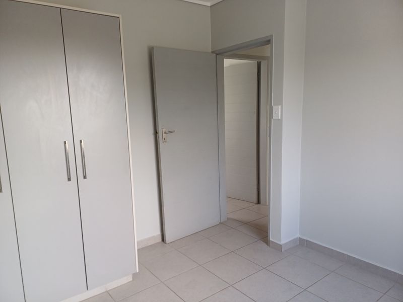 A clean, neutral bedroom featuring built-in cupboards, tiled flooring, and a doorway leading to an adjacent room.