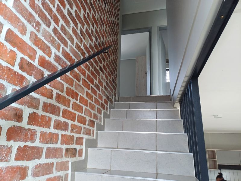 A staircase featuring tiled steps, a metal handrail, and an exposed brick feature wall leading to an upper landing.