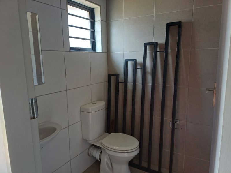 A compact bathroom featuring tiled walls, a standard toilet, and a small wall-mounted basin with a window for natural light.