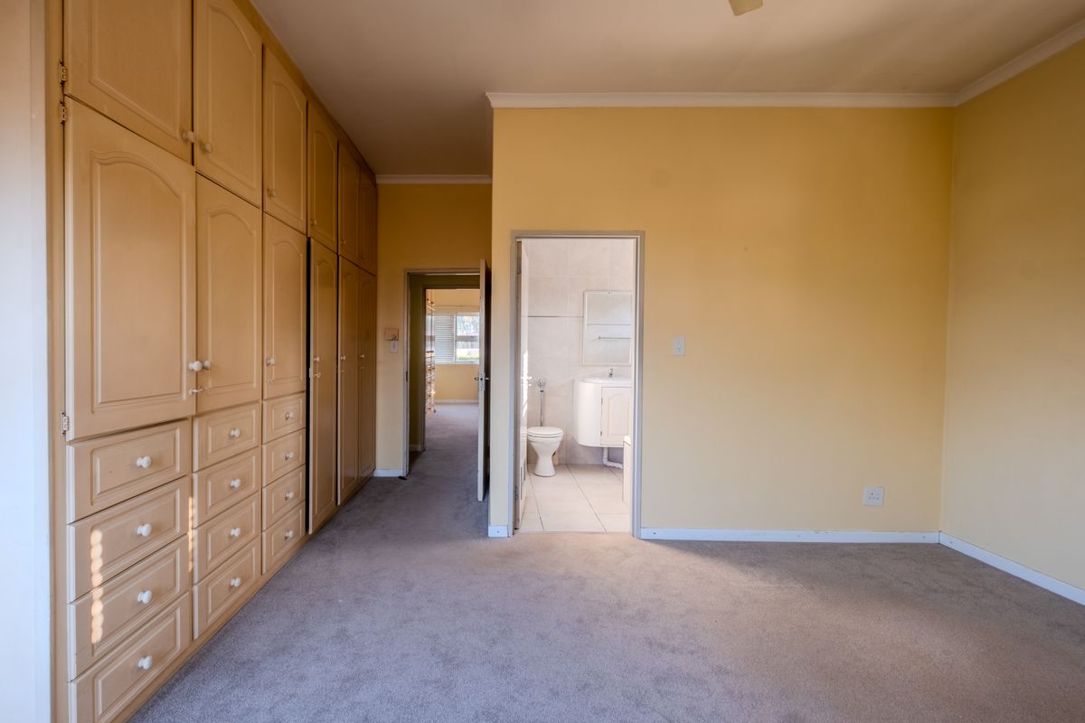 Spacious bedroom featuring extensive built-in cabinetry, neutral carpeting, and direct access to an en-suite bathroom.