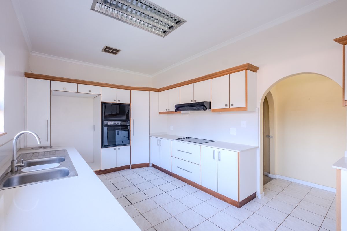 A functional, empty kitchen featuring white cabinetry, built-in oven, electric hob, extractor fan, and tiled flooring, leading through an archway to adjacent space.