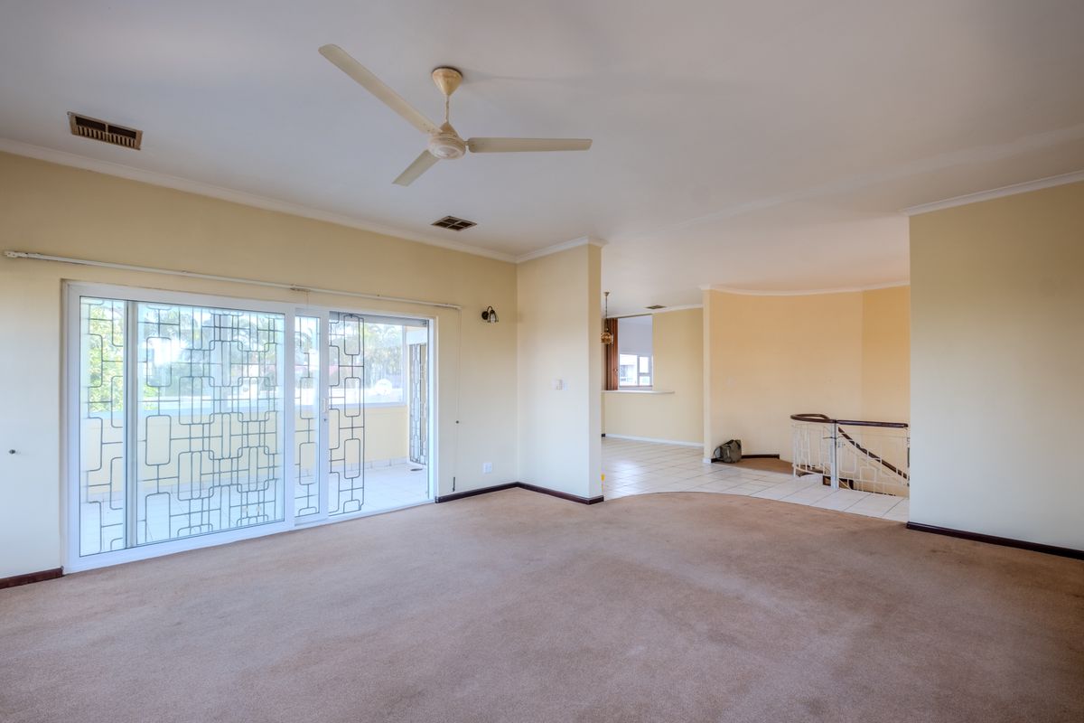 Spacious, empty living area featuring neutral carpeting, a ceiling fan, and sliding glass doors leading to an outdoor space.