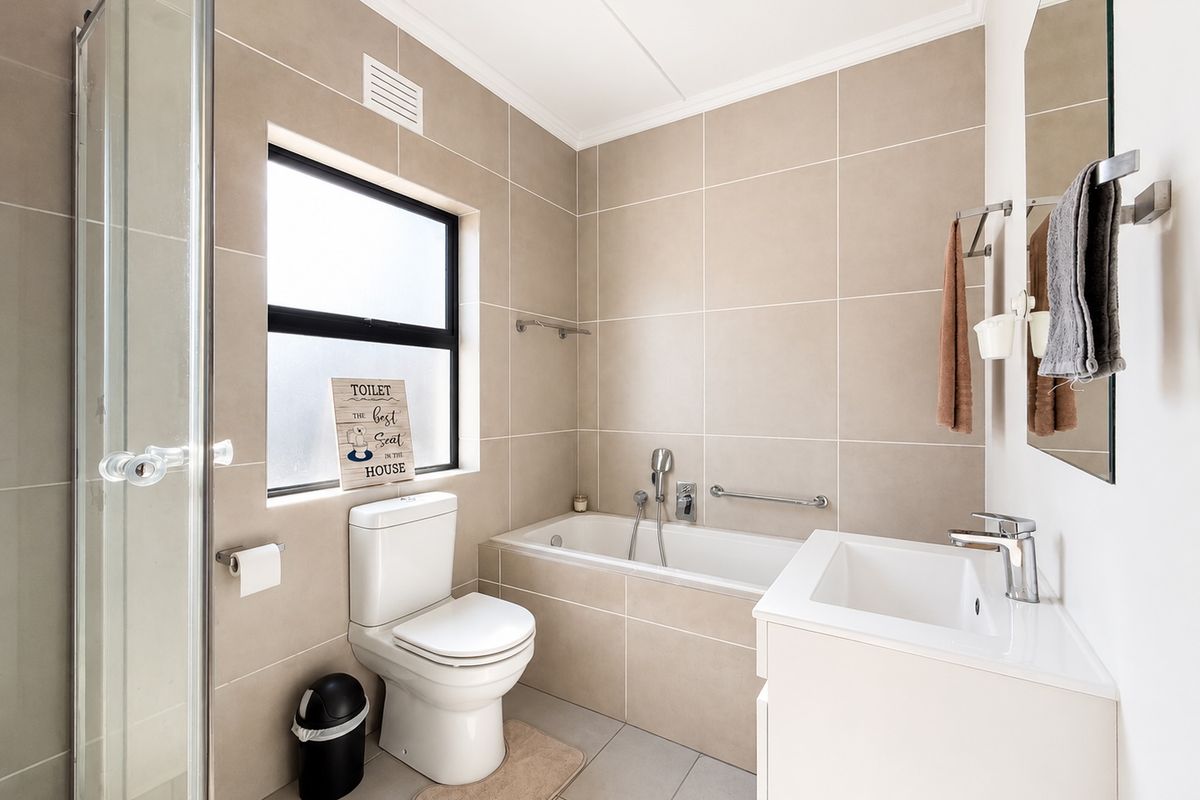 A modern, well-maintained bathroom featuring a shower enclosure, bathtub, vanity basin, and neutral floor-to-ceiling wall tiling.