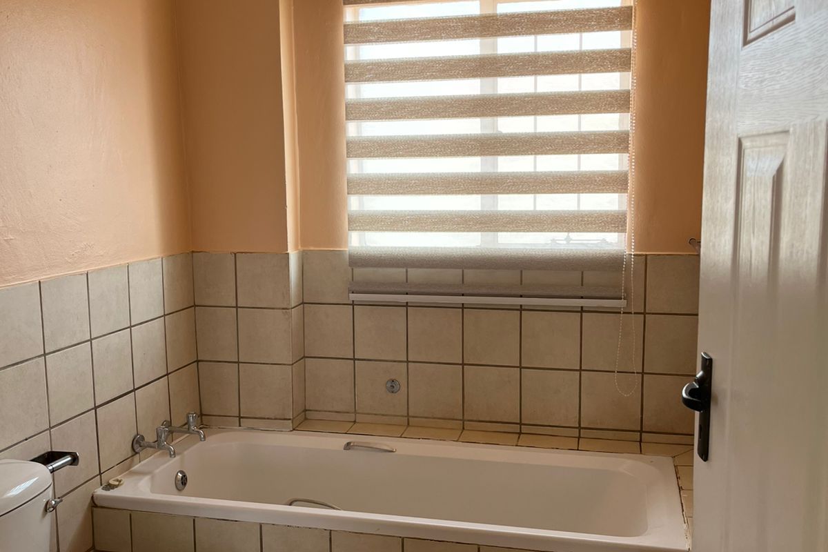 A functional bathroom featuring a built-in bathtub, ceramic tiling, and a window with a roller blind.