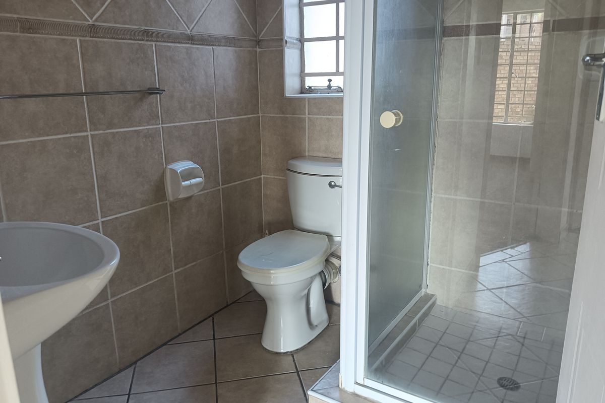 A functional bathroom featuring a pedestal basin, toilet, and a glass-enclosed shower with neutral ceramic wall and floor tiling.