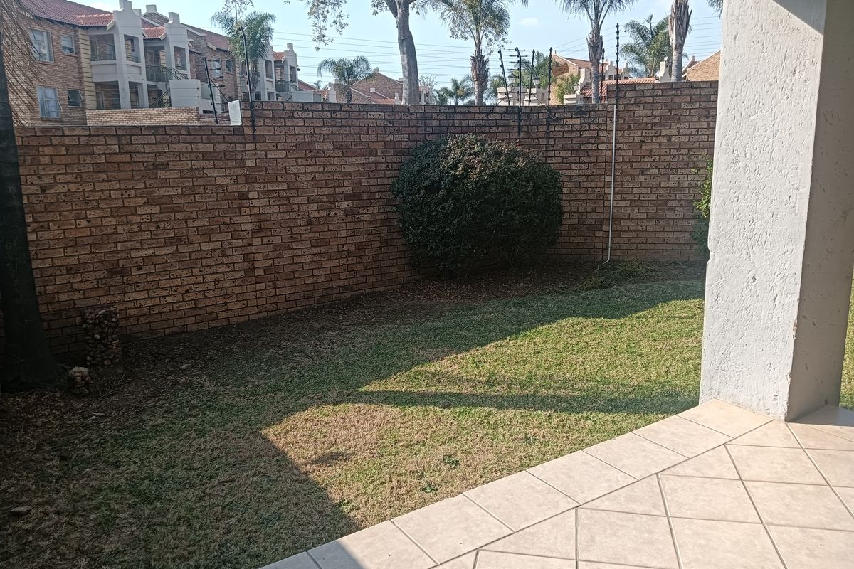 A private rear garden featuring a tiled patio area, established lawn, and secure brick boundary wall with electric fencing.