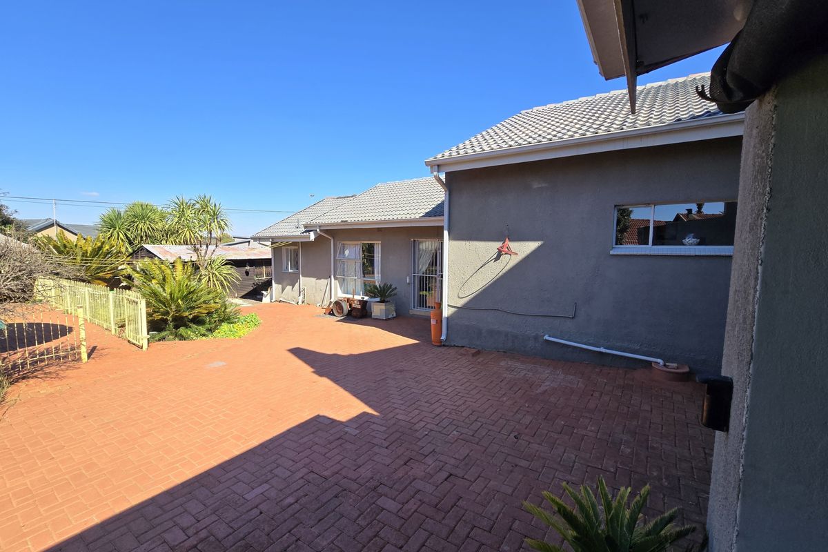 A rear exterior view of the property featuring a paved courtyard area, tiled roof, and access to the home via a security gate.