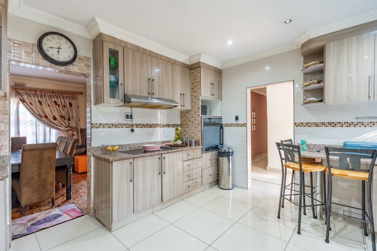 A well-maintained kitchen featuring light wood-finish cabinetry, granite countertops, built-in oven, and a breakfast bar area with tiled flooring throughout.