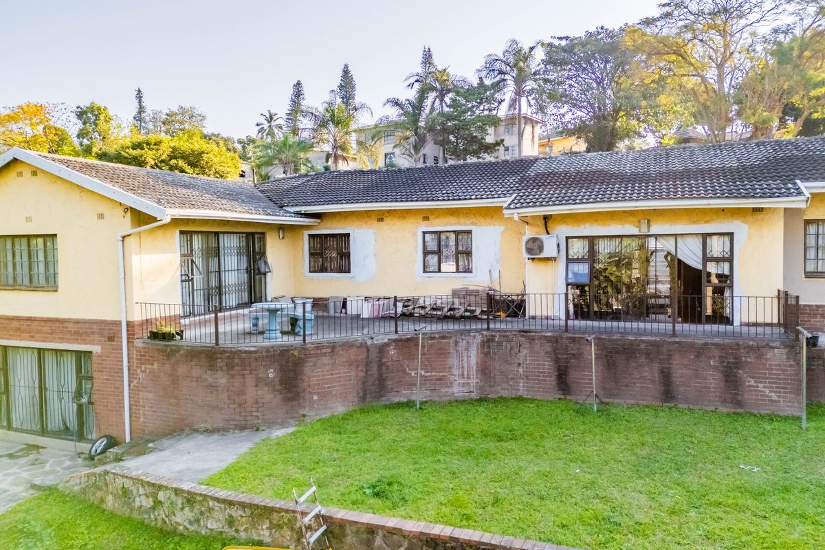 Rear view of the house featuring a raised patio, brick retaining wall, and tiled roof, showing signs of exterior wear and maintenance needs.
