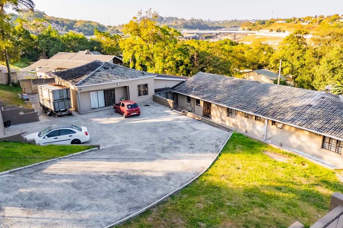 Aerial view of the property showing the main dwelling, extensive concrete driveway, and surrounding landscaped grounds.