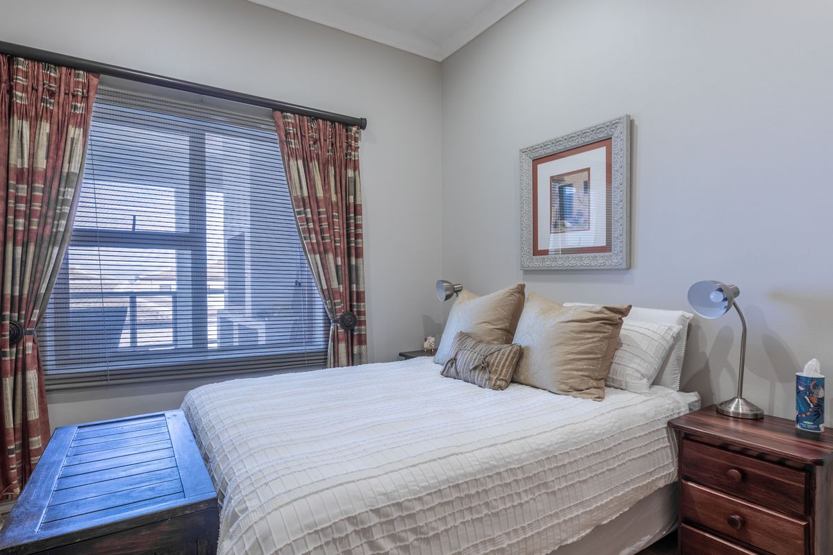 A well-maintained bedroom featuring neutral wall tones, a large window with fitted blinds and curtains, providing natural light and a comfortable living space.