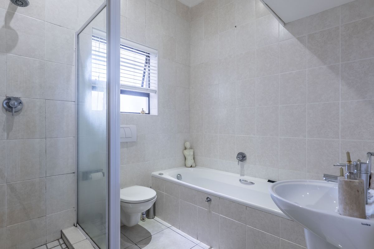 A clean, modern bathroom featuring a glass-enclosed shower, a built-in bathtub, a wall-mounted toilet, and a pedestal basin with neutral wall and floor tiling.