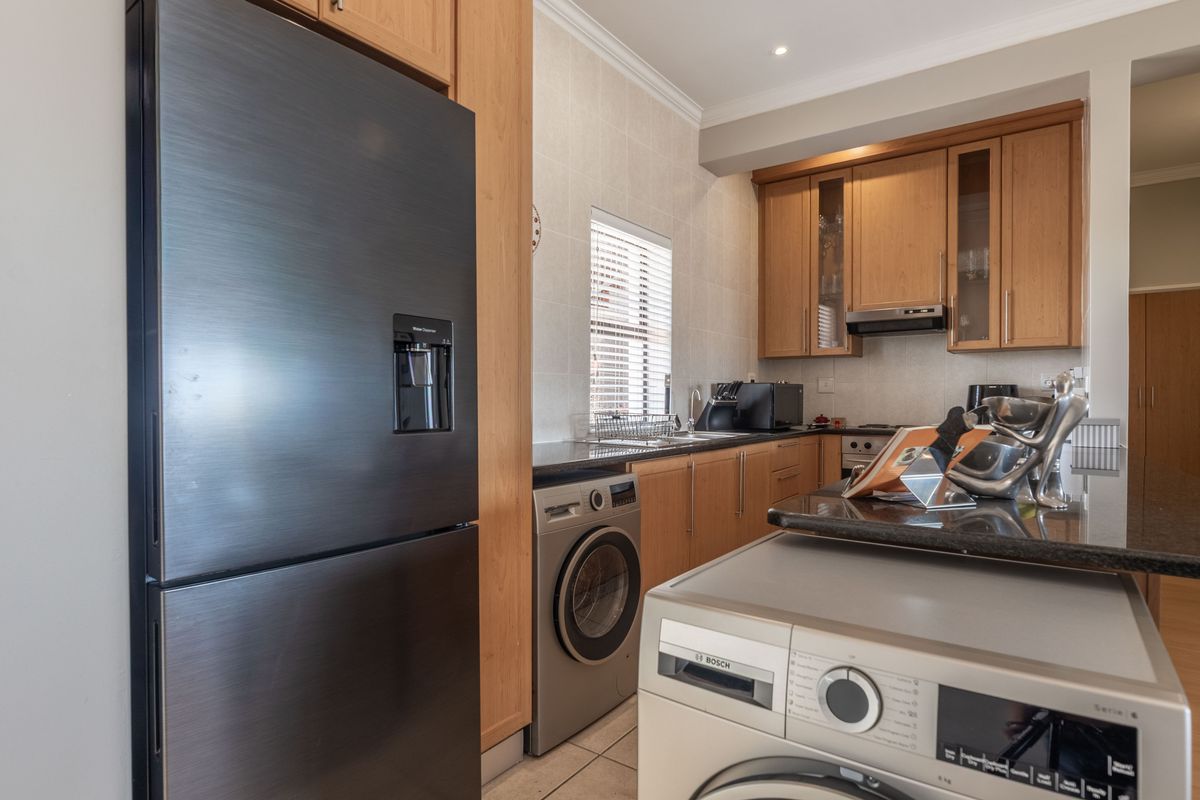 A functional kitchen featuring wooden cabinetry, granite countertops, a tiled backsplash, and integrated appliances, offering a practical layout for daily cooking and laundry needs.
