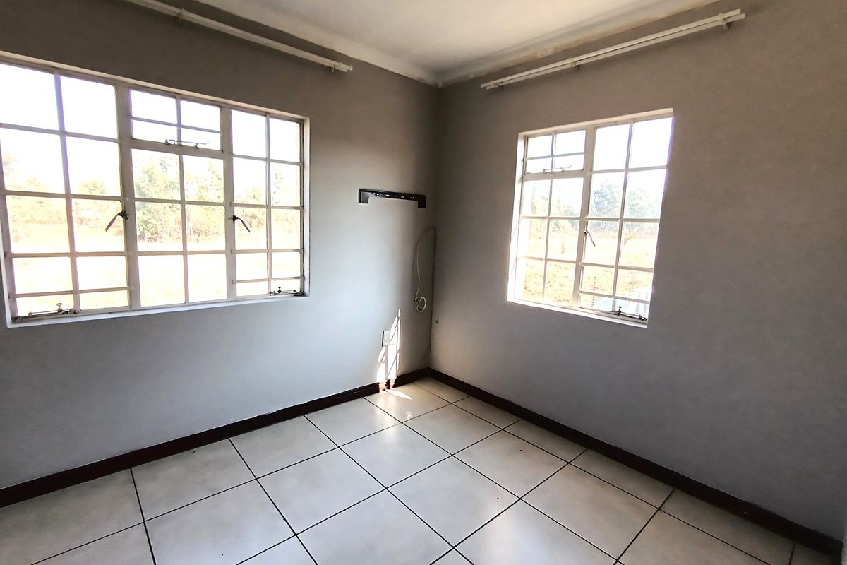 A vacant bedroom featuring tiled flooring, large windows with security bars, and neutral wall finishes, providing a blank canvas for personalization.