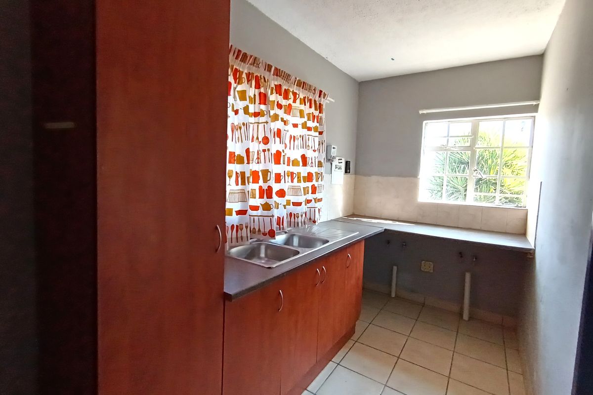 A functional kitchen area featuring built-in wooden cabinetry, a double sink, tiled flooring, and a window providing natural light.