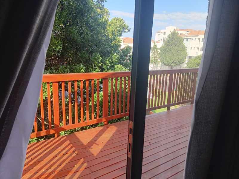 A wooden balcony with a timber balustrade, accessible via a sliding glass door, offering an elevated outdoor space.