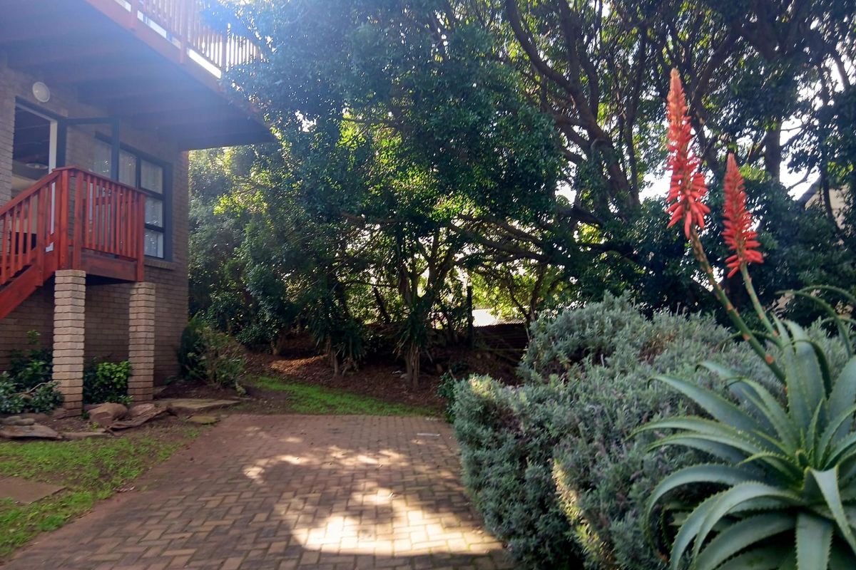 Rear exterior view of the cottage featuring a brick-paved patio area, mature garden landscaping, and an elevated timber deck with balustrade.