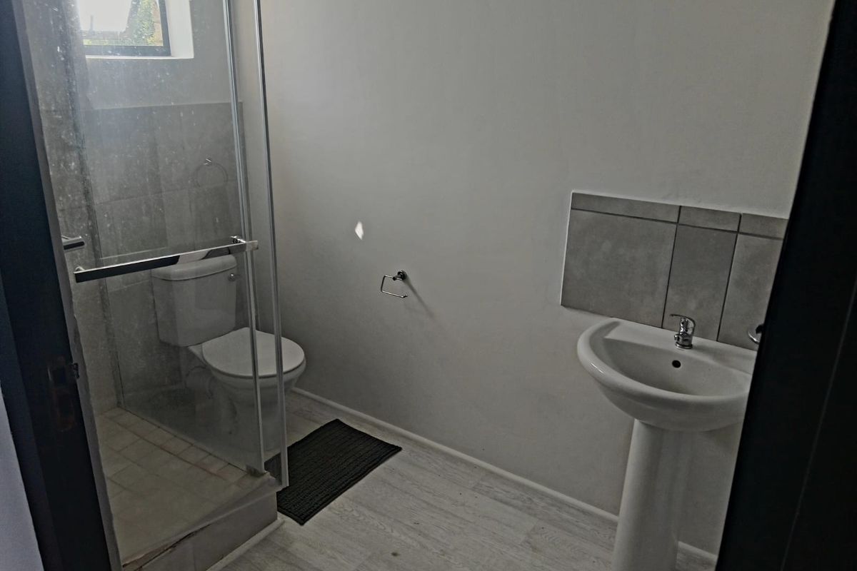 A functional bathroom featuring a glass-enclosed shower, pedestal basin, and toilet with neutral wall finishes and tiled splashback.