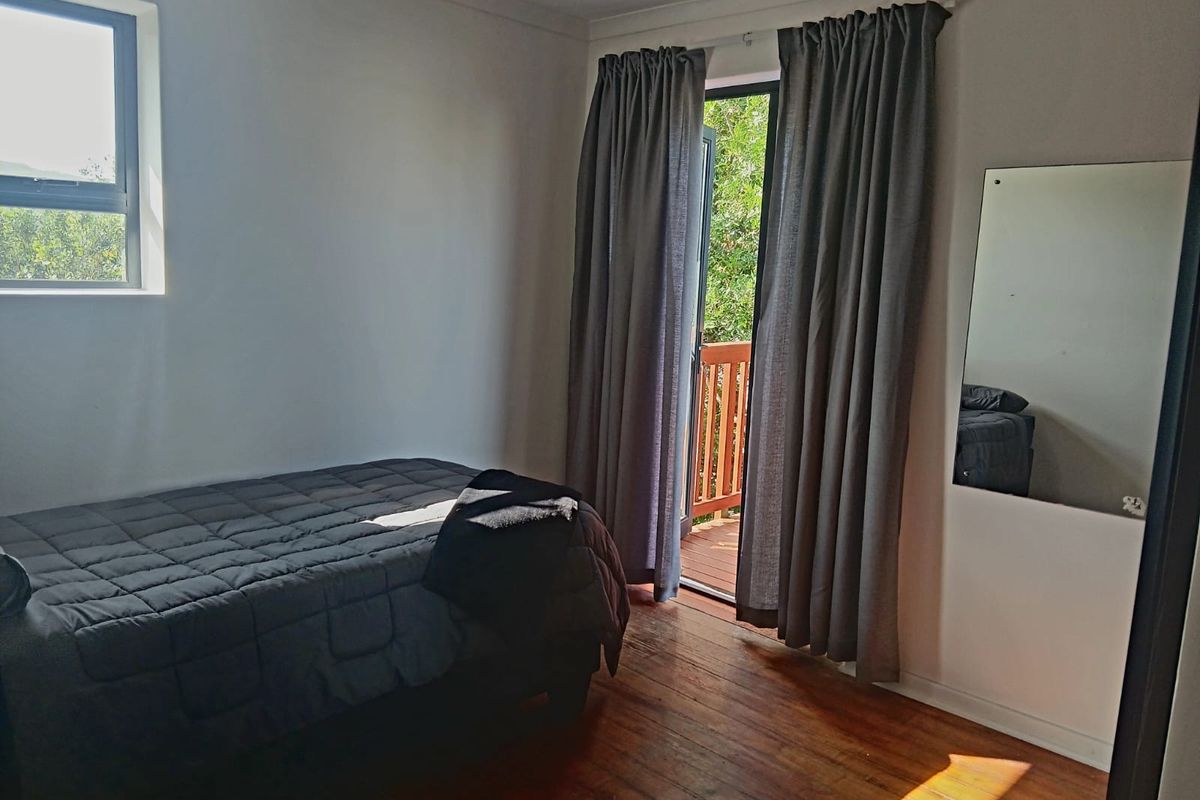 A bedroom featuring polished timber flooring, a large window, and a sliding door providing direct access to an outdoor balcony area.