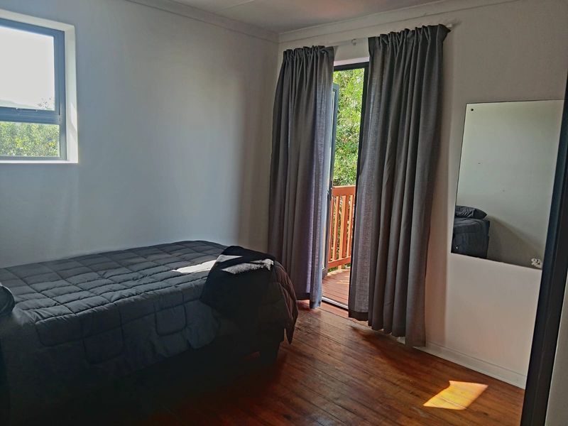 A bedroom featuring polished timber flooring, a large window, and a sliding door providing direct access to an outdoor balcony area.
