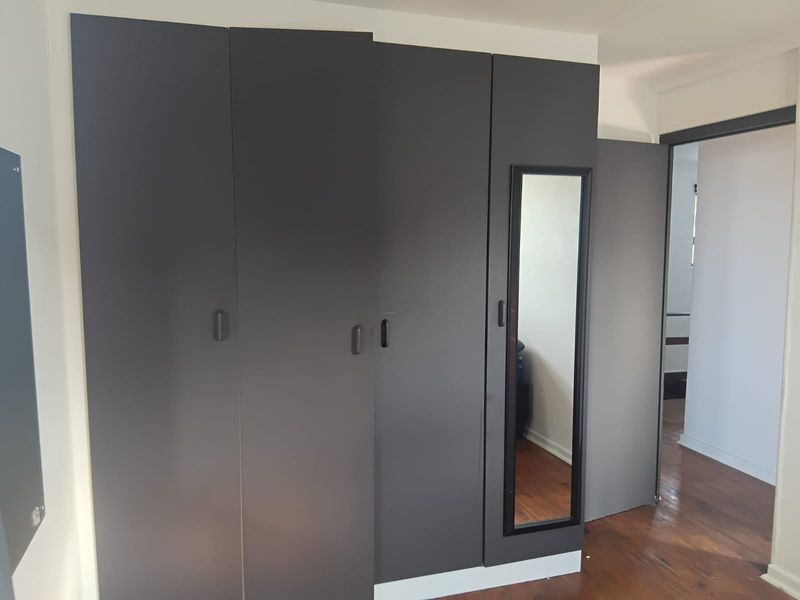 A bedroom featuring dark grey built-in wardrobes with a full-length mirror and polished hardwood flooring.