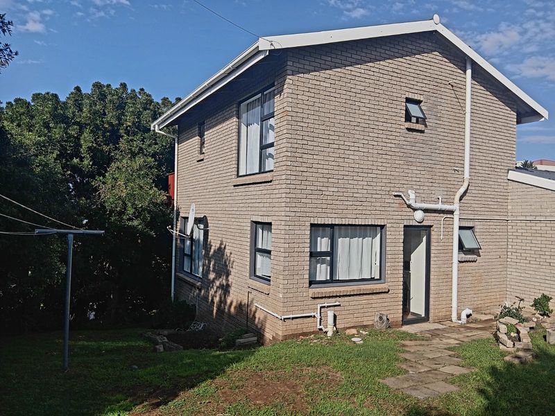 Rear view of a two-story brick cottage featuring aluminium window frames, external plumbing fixtures, and a paved garden walkway.