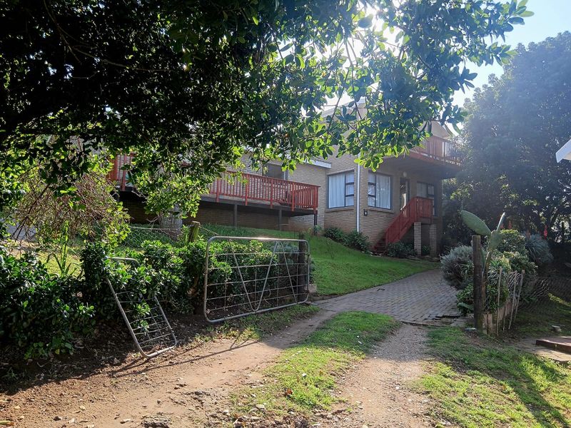 Front view of a cottage featuring a brick facade, elevated timber deck, and a paved driveway leading to the entrance.